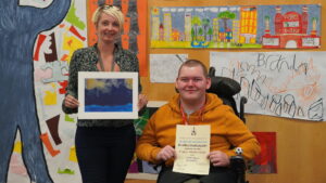 Bradley with his Art Tutor Leanne showing his winning certificate and artwork